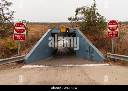 Bright red Do Not Enter and Wrong Way signs on both sides of Tunnel / underpass with white speed bump and guard rails leading under railroad tracks. Stock Photo