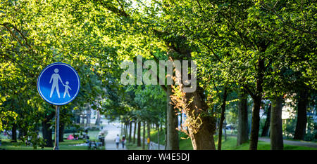 Attention, children crossing. White mother holding a child icon on round blue color sign, green trees outdoors background. Dutch road sign, Rotterdam Stock Photo