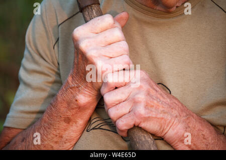 Closeup of a very old mans or womans hands are holding an old gnarled stick instead of a cane Stock Photo