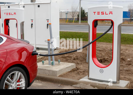 Closeup of red Tesla Model S plugged-in, charging at a Tesla Supercharger Stall in Mississauga, Ontario. Stock Photo