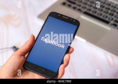 Nizhyn, Ukraine/July-16-2019: Girl hold smartphone and use Facebook application. Social media concept. Stock Photo