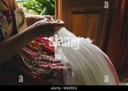 Female seamstress patching a wedding dress with thread and needles in a handmade way at home. Stock Photo