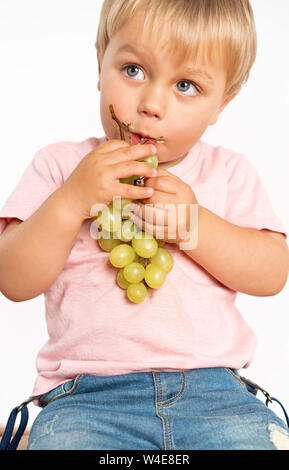 Baby boy eating grapes in the studio isolated on white background. Concept healthy fresh food Stock Photo