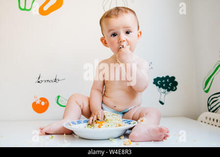 Baby eating by himself learning through the Baby-led Weaning method, exploring the flavors of food with curiosity. Stock Photo