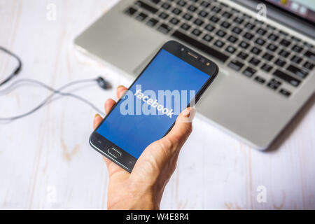 Nizhyn, Ukraine/July-16-2019: Young girl hold smartphone in her hand with Facebook application launched. Social media concept. Stock Photo