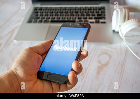 Nizhyn, Ukraine/July-16-2019: Young man in black suite hold smartphone and use Facebook app. Social media and corporative concept. Stock Photo