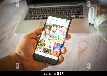 Nizhyn, Ukraine/July-16-2019: Young man in black suite hold smartphone and use Instagram app. Social media and corporative concept. Stock Photo