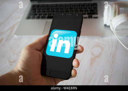 Nizhyn, Ukraine/July-16-2019: Young man in black suite hold smartphone and use Linkedin app. Social media and corporative concept. Stock Photo