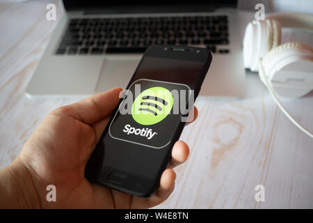 Nizhyn, Ukraine/July-16-2019: Young man in black suite hold smartphone and use Spotify app. Social media and corporative concept. Stock Photo
