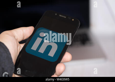 Nizhyn, Ukraine/July-16-2019: Young representative man in black suite hold smartphone and use Linkedin app. Social media and corporative concept. Stock Photo