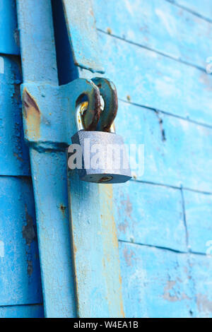 old padlock on a blue metal door with wooden planks cracked paint and rust Stock Photo