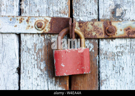 Old brown padlock on a gray door with wooden planks of cracked paint and rust. Vintage gates with metal stripes and bolts Stock Photo