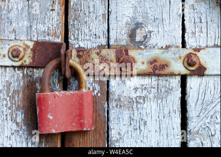 Old brown padlock on a gray door with wooden planks of cracked paint and rust. Vintage gates with metal stripes and bolts Stock Photo