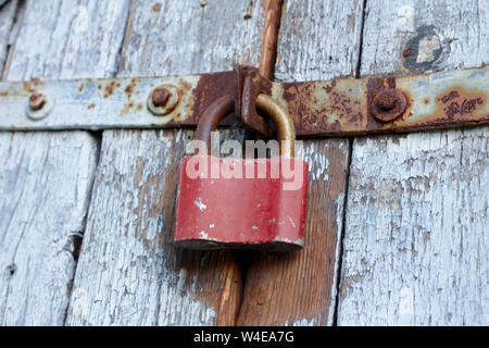 Old brown padlock on a gray door with wooden planks of cracked paint and rust. Vintage gates with metal stripes and bolts Stock Photo