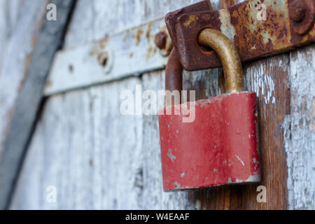Old brown padlock on a gray door with wooden planks of cracked paint and rust. Vintage gates with metal stripes and bolts