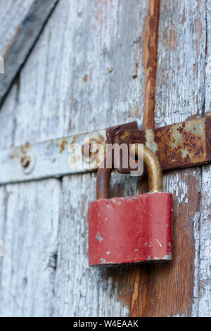 Old brown padlock on a gray door with wooden planks of cracked paint and rust. Vintage gates with metal stripes and bolts Stock Photo