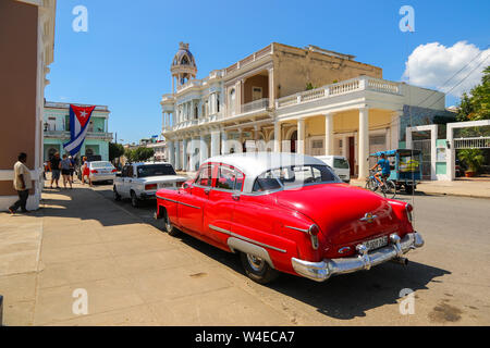 Cienfuegos, Cuba - Red vintage american car on the Plaza Jose Marti with Ferrer Palace in the background Stock Photo