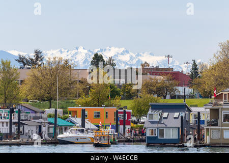 On the water homes/shops and boats in Victoria, BC with snow covered mountains in the background. Stock Photo