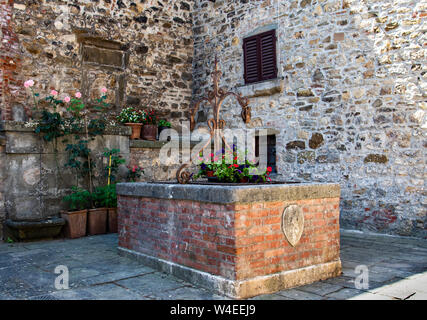 Brick garden centerpiece with flowers in the middle of a stone courtyard in Tuscany, Italy Stock Photo