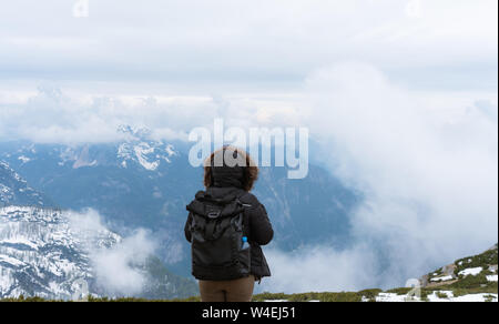 Traveler woman with backpack looking at Alpine mountain view from mountain peak with sky full of cloud Stock Photo