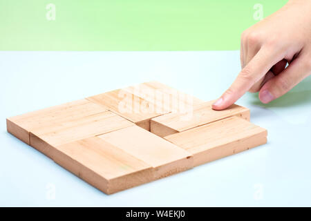 Hand put a wooden block into place on the table over green background Stock Photo