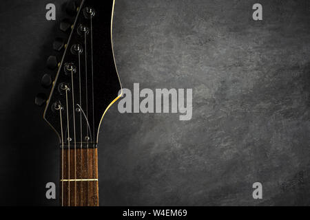 Headstock of black electric guitar on black cement floor. Top view and copy space for text. Concept of rock music. Stock Photo