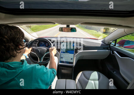 Full front view of man driving Red Tesla Model S with navigation on screen beside. Interior covered in black and grey leather. Stock Photo