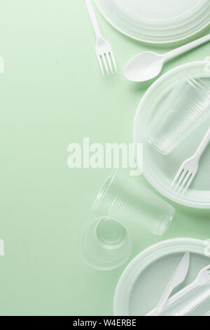 White plastic disposable tableware on green background. Copy space. Stock Photo