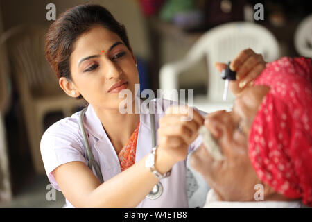 Female doctor putting eye drops in a old man eye Stock Photo
