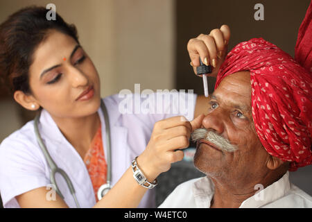 Female doctor putting eye drops in a old man eye Stock Photo