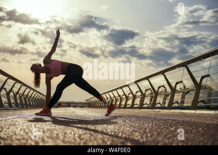 Morning workout. Full-length of young disabled woman with leg prosthesis in sportswear doing yoga exercises while standing on the bridge. Disabled sport concept. Motivation. Healthy lifestyle Stock Photo