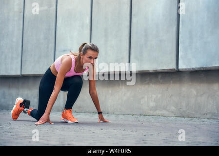 I am ready Beautiful disabled woman with leg prosthesis in sports clothing standing on the start line while running outdoors. Disabled sport concept. Motivation. Healthy lifestyle Stock Photo