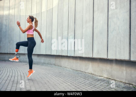 No limits Active disabled woman with leg prosthesis in sports clothing jumping while her morning workout outdoors. Disabled sport concept. Motivation. Healthy lifestyle Stock Photo