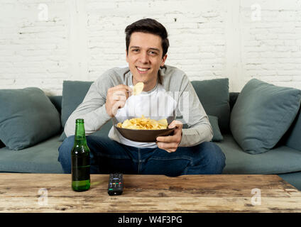 Lifestyle portrait of young man on sofa watching sports or exciting movie on television. Having fun at home enjoying and celebrating goal and victory Stock Photo