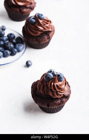 Homemade chocolate cupcakes with buttercream and blueberries on white table, close up, delicious festive dessert or breakfast Stock Photo