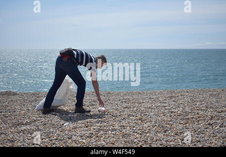 Man being environmentally conscious by clearing discarded litter and single use plastic waste from a British Beach Stock Photo