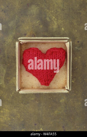 Knitted red woollen heart lying in small cardboard box on tarnished brass Stock Photo