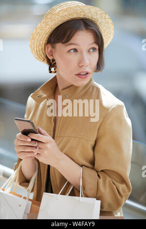 Content beautiful young woman with short hair wearing straw hat and beige jacket checking shopping promotions via mobile app Stock Photo