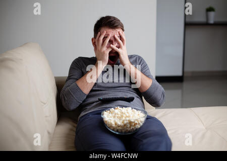 Scared man watching tv hiding his eyes Stock Photo
