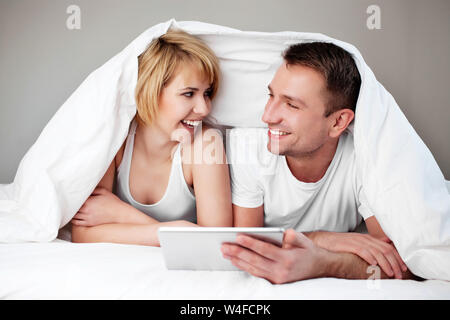 Happy couple lying in bed with digital tablet Stock Photo