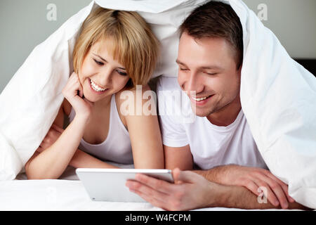 Happy couple lying in bed with digital tablet Stock Photo