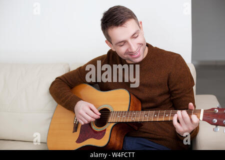 Handsome young man playing guitar, sitting on sofa Stock Photo