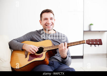 Handsome young man playing guitar, sitting on sofa Stock Photo