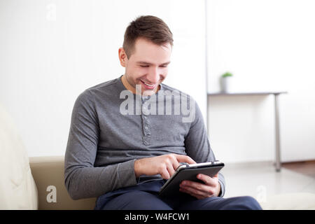 Handsome man using digital tablet, sitting on a couch and smiling Stock Photo