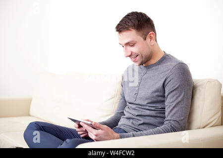 Handsome man using digital tablet, sitting on a couch and smiling Stock Photo