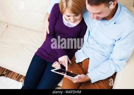 Young hugging  couple sitting on a sofa and using a digital tablet Stock Photo