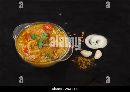 Red lentil soup in a glass plate with spices, herbs, onion and garlic on a black background Stock Photo