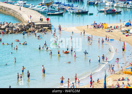 Lyme Regis, Dorset, UK. 23rd July 2019. UK Weather: Holidaymakers flock to the picturesque seaside resort of Lyme Regis to soak up the scorching hot sunshine and on the first week of the school summer holidays. Visitors arrive early to secure a spot on the beach to swelter in the hot sunshine on the town's packed beach while others take a cooling dip in the sea on what is set to be the hottest week of the year so far as the African Plume hits southern Britain. Credit: Celia McMahon/Alamy Live News. Stock Photo