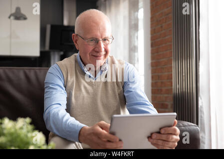 Elderly man using tablet PC. Senior sitting on sofa in living room Stock Photo