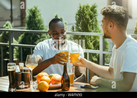 Young group of friends drinking beer, having fun, laughting and celebrating together. Smiling men with beer's glasses in sunny day. Oktoberfest, friendship, togetherness, happiness, summer concept. Stock Photo